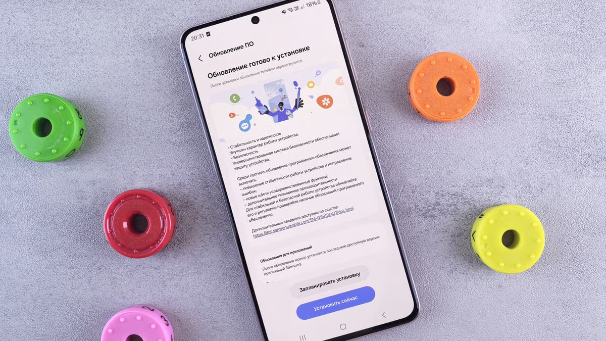 Flat lay of a smartphone displaying a software update, surrounded by colorful toy accessories on a gray desk.